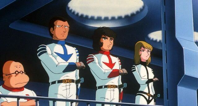 Four characters from the old anime “star blazers”, They are saluting with the right arm across the chest. From left to right, 
Docor Sane, a short bald man with glasses
Sandor, a tall man in white and blue uniform
Derek Wildstar, a man with shaggy brown hair and white and red uniform 
Nova, a brown haired woman in white and black uniform. 
