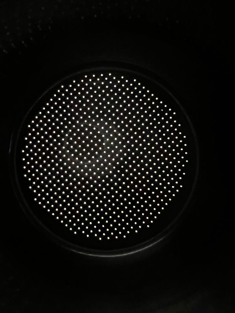 The bottom of an espresso back skit taken from the inside, so it’s pitch black except for light is coming through the holes. Here the holes don’t go all the way to the edges of the bottom. The whole pattern is also a grid.
