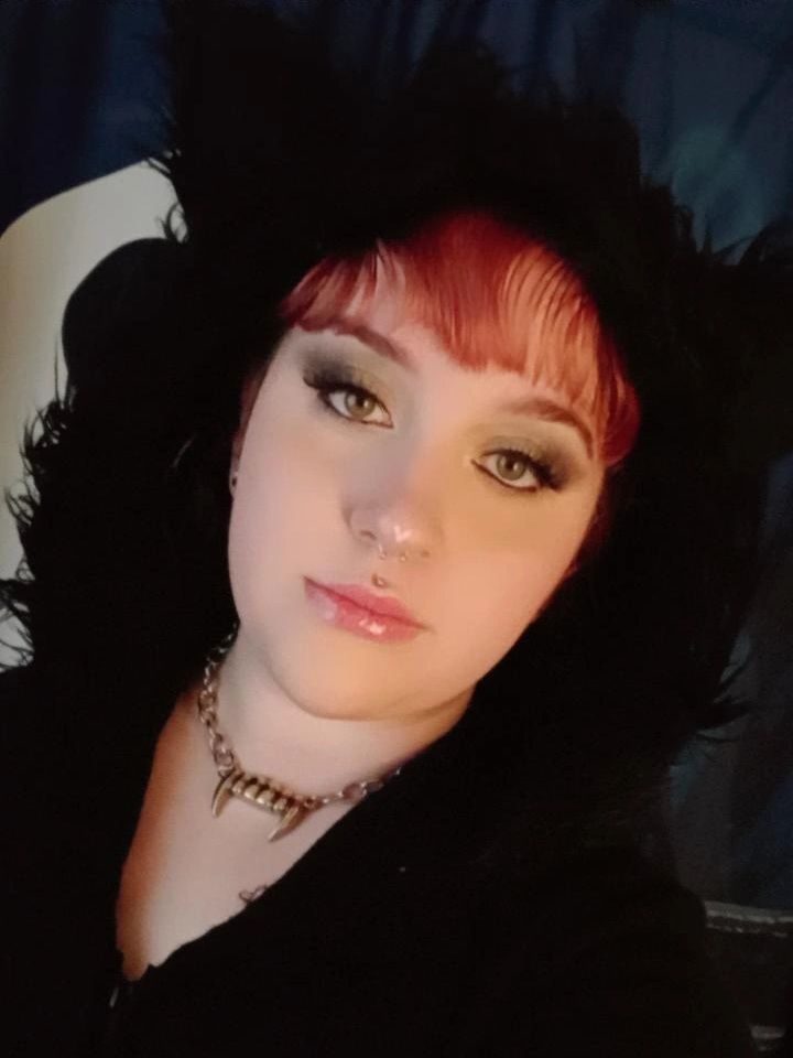 Selfie of me in a black bat costume with a fluffy hood , a silver vampire fang necklace and dark grey eyeshadow 