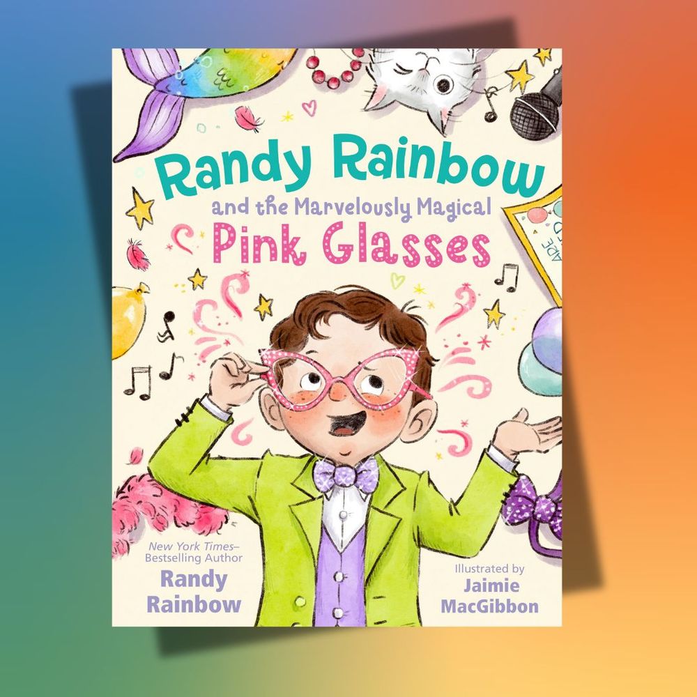 A picture book cover on a rainbow background. The book cover depicts an elementary school aged boy in a green and purple wearing sparkly bedazzled pink cat eye glasses. He has brown hair and eyes and a light complexion with ruddy cheeks. He is surrounded by various items, including a rainbow mermaid tale, a white cat, a microphone, a yellow balloon, a pink feather boa, and a purple sparkly bowtie.  The book title is: Randy Rainbow and the Marvelously Magical Pink Glasses by Randy Rainbow, illustrated by Jaimie MacGibbon. 