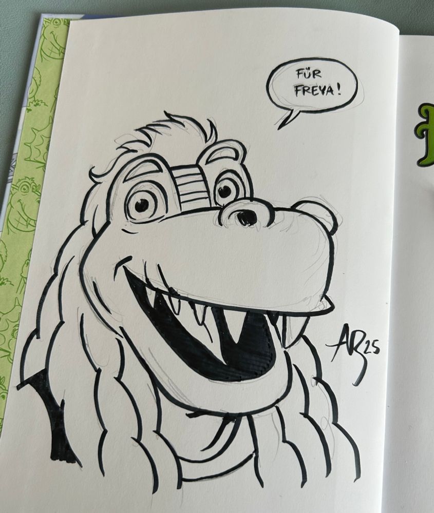 Signature and drawing of a cartoony dinosaur in a book 