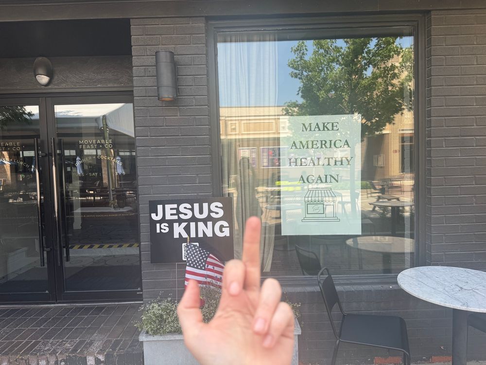 A restaurant window has a poster that reads “Make America Healthy Again” alongside another sign that says “Jesus is king.”