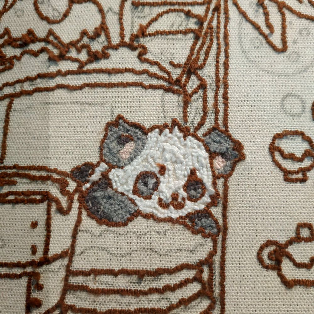 Parte traseira de um tapete bordado em ponto russo. A única parte bordada nessa imagem é um filhote de panda deitado de barriga para baixo. Seu pelo vai de branco a duas variações de cinza.