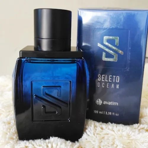 Imagem do frasco do perfume seleto Ocean em cima de um tapete branco com sua caixa atrás do frasco 