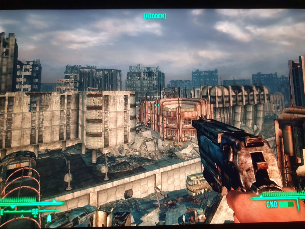 The Lone Wanderer in first-person mode on top of a tall structure (?), possibly a bridge or a rooftop, overlooking the Capital Wasteland.