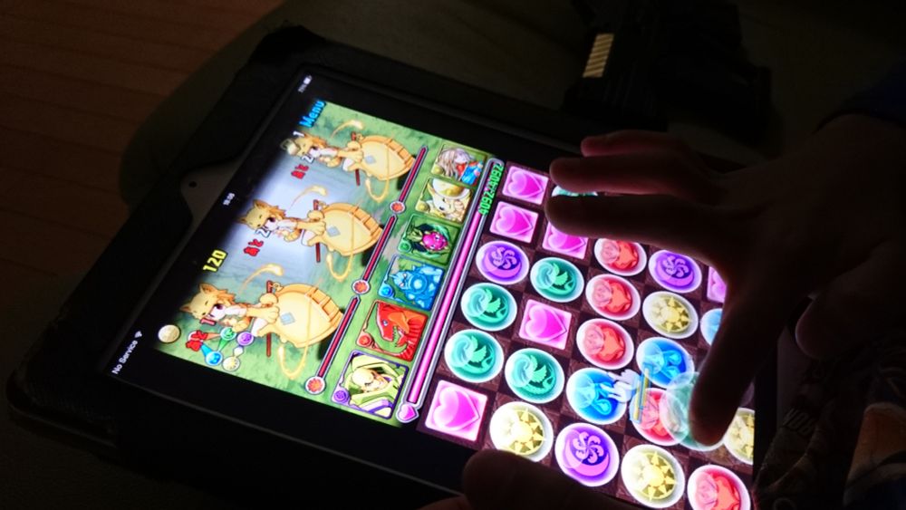 A picture of the game Puzzle & Dragons on an iPad. Three Moonlight Flowers from Ragnarok Online are on the top screen of the game. A child's hand can be seen on the lower right corner, playing the game.