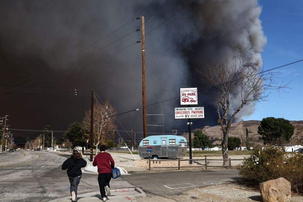 People hustle down a sidewalk as the Hughes Fire burns north of Los Angeles, near Castaic. Photo by Mario Tama for Getty Images.
