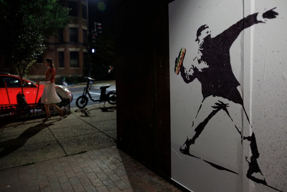 A DOJ employee was fired and charged with a felony after chucking a footlong at a federal agent. Now his likeness is a symbol --- and for sale on t-shirts.