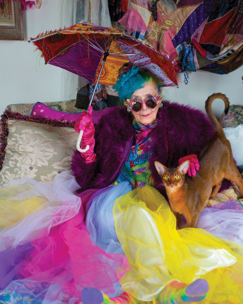 Emily is photographed with her cat, Kitties, holding a vibrant umbrella and wearing sunglasses. The image is featured in Ari Seth Cohen's new book, "Advanced Pets."