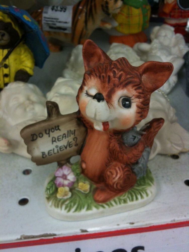I think it’s a ceramic fox with its tongue out holding a sign that says do you really believe. Might be a dog. 