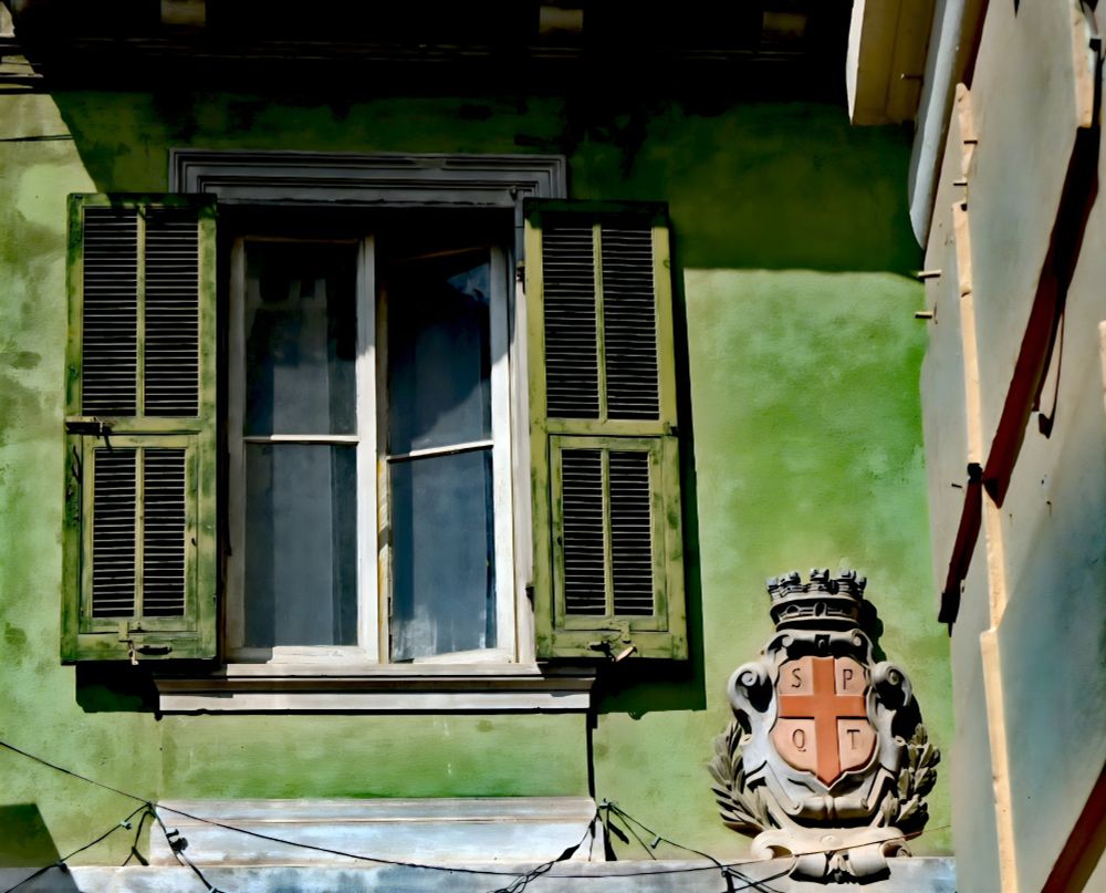 Altstadtdetail: Fenster auf grüner Hauswand. Daneben ein verschnörkeltes Hoheitszeichen. Rechts die Ecke des Nachbarhauses.
