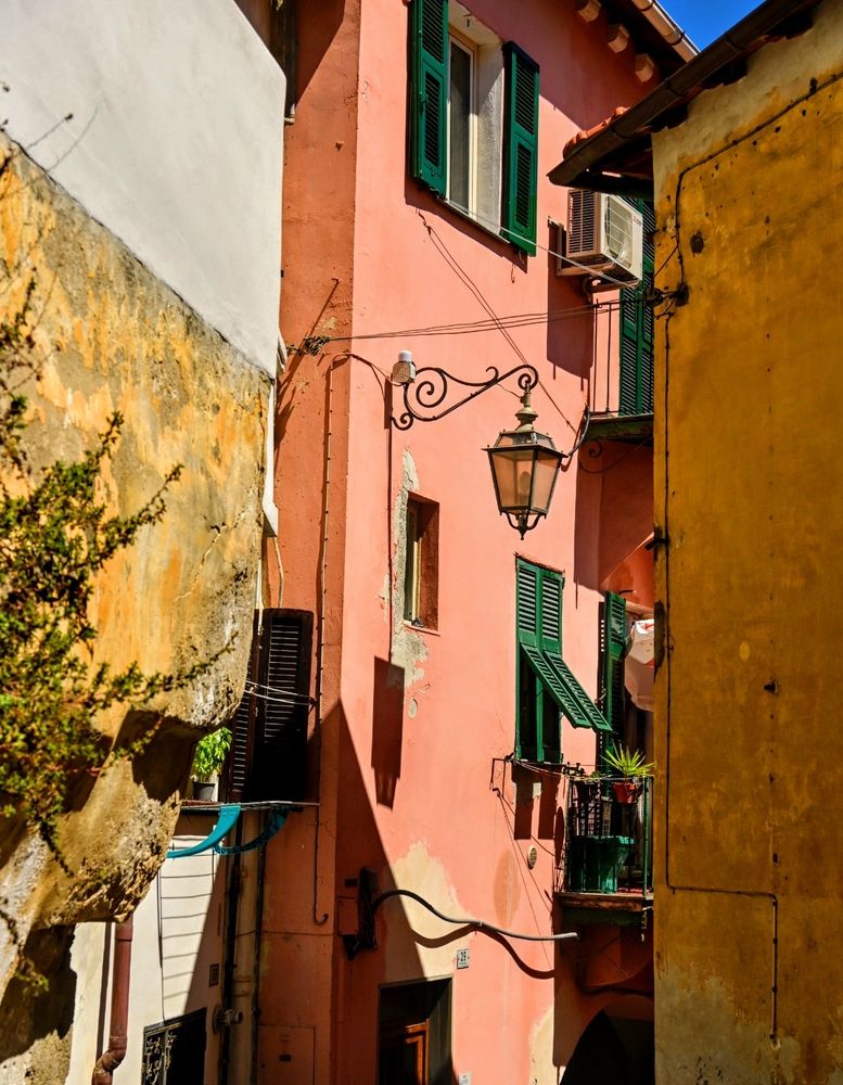 Ecke eines Sonne beschriebenen roten Altstadt Hauses südländischer Architektur.  Eingerahmt von anderen Hausecken. In der Mitte eine schöne Steassenlaterne 