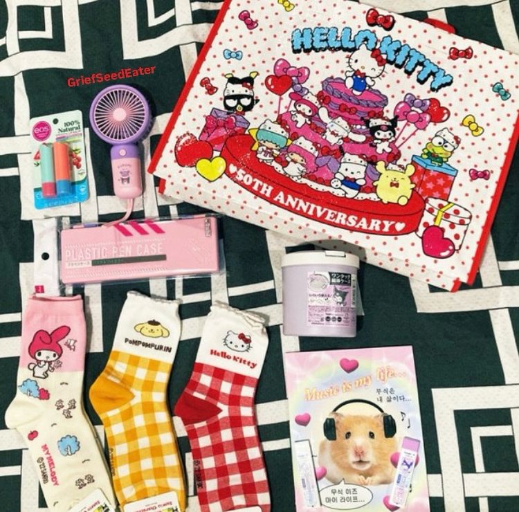 Image featuring the following items:
- Eos lip balm
- Kuromi Portable Fan
- Reusable Hello Kitty 50th Anniversary Shopping Bag
- Multicolored Pencil Case
- Kuromi Q-Tip Container
- 3 Pairs of Socks: My Melody, Pompompurin & Hello Kitty
- Tacky Notebook with a cover featuring a hamster with headphones that says “Music is my life…”