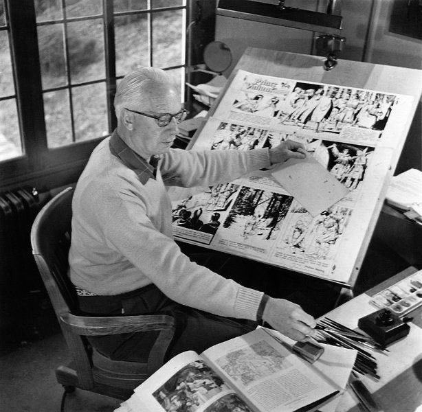A black and white photo of Foster at his drawing table with a huge page of original art.