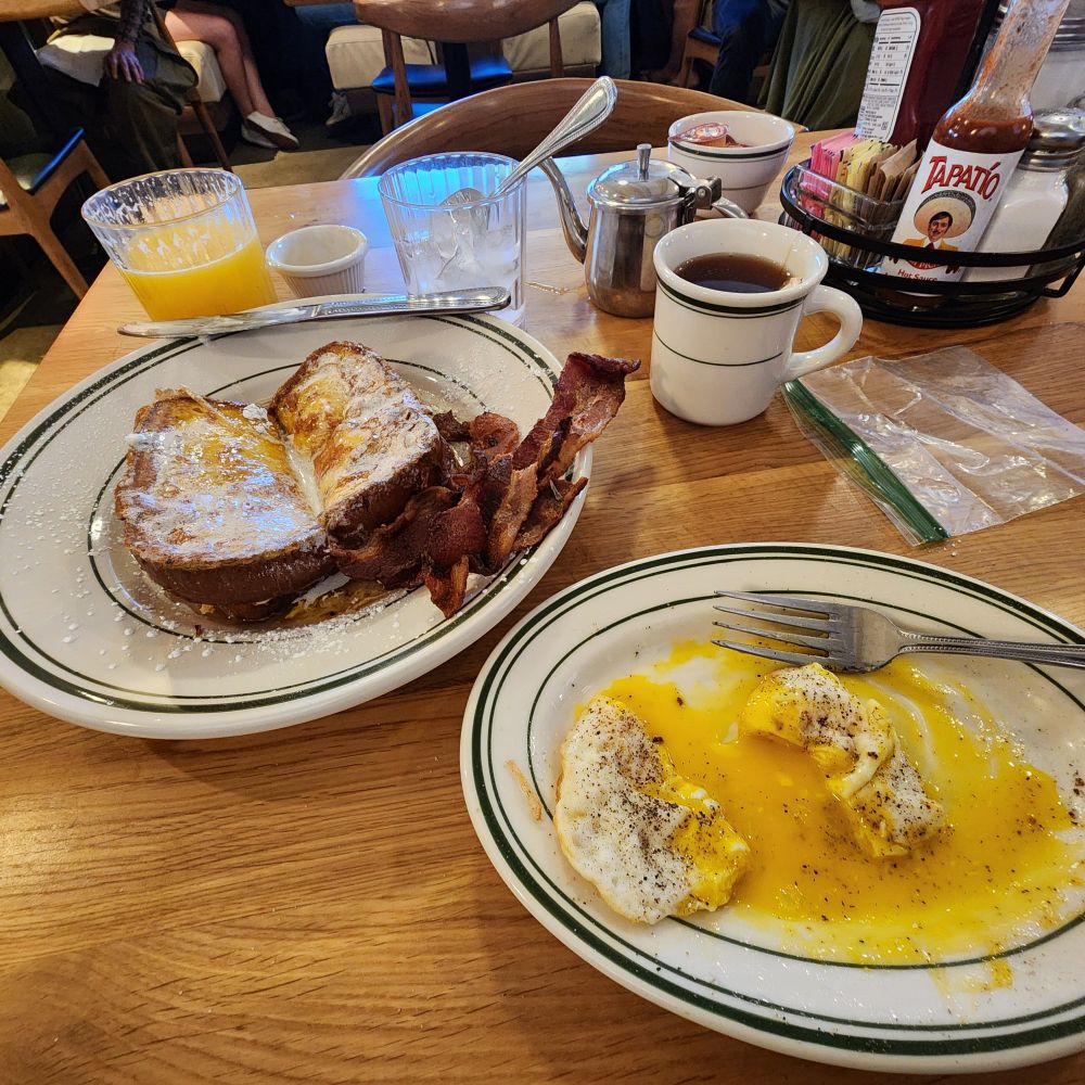 Table with eggs over easy, bacon 🥓 and French toast. 😋 Also hot tea and orange juice. Yum!!