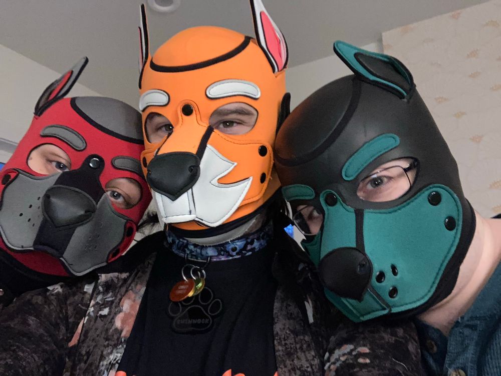 Selfie of three human pups, a red one, an orange one, and a teal one 