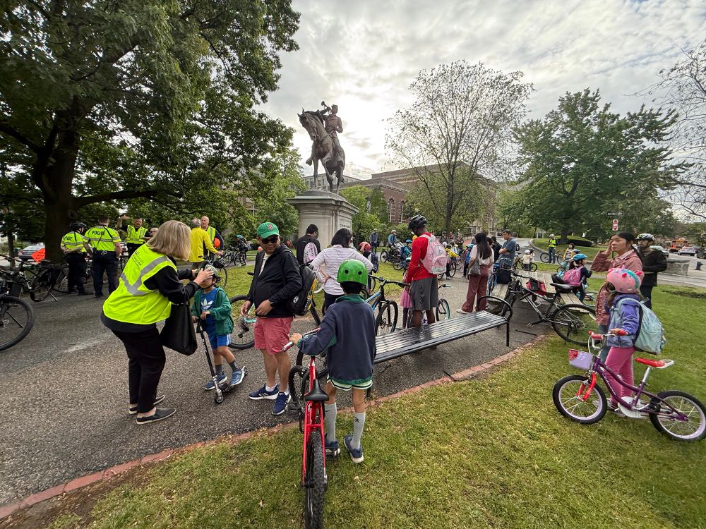 Students and community members wait for the start of the Pierce bike bus. Tina from the state Safe Routes to Schools group adjusts a student’s helmet for a safe fit.