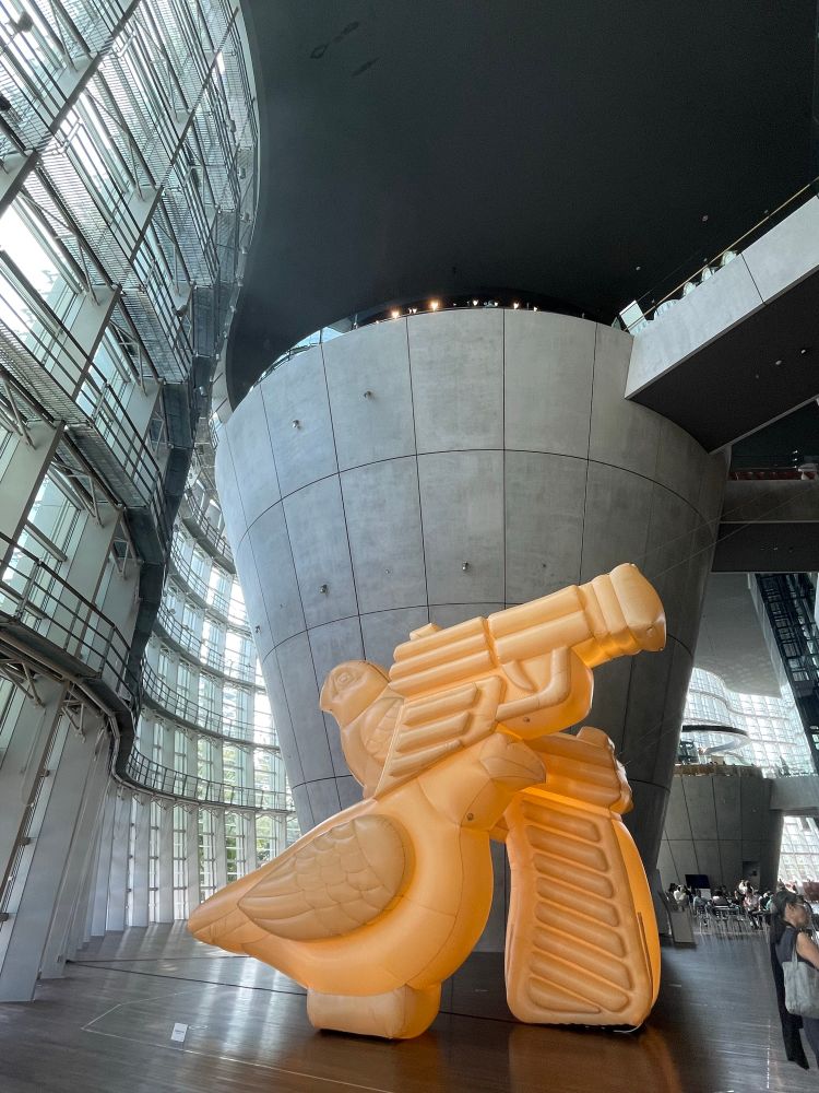 美味しそうで合ってた。ベビーカステラモチーフ。
胡宮 ゆきな
平和なんて朝飯前（10XL） vs 平和なんて朝飯前（10XL）

＜平和なんて朝飯前（IT'SAPEACE OF CAKE）＞は、“Piece”を“Peace”に置き換えた造語です。
台湾の夜市で見た雞蛋糕（ベビーカステラ）の袋の中に、銃と鳩といった相反する象徴が共存していた光景は、矛盾が無自覚に消費される現代の構造を想起させました。
可食素材とインフレータブルという異なるスケールのメディアを通して、身体を起点に思想や欲望が取り込まれるプロセスを可視化させ、世界の複雑さとその脆弱性に改めて目を向けます。