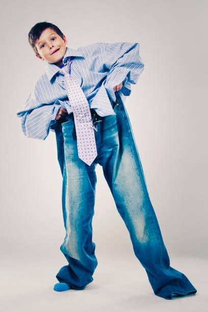 A kid wearing comically oversized pants, dress shirt, and tie.