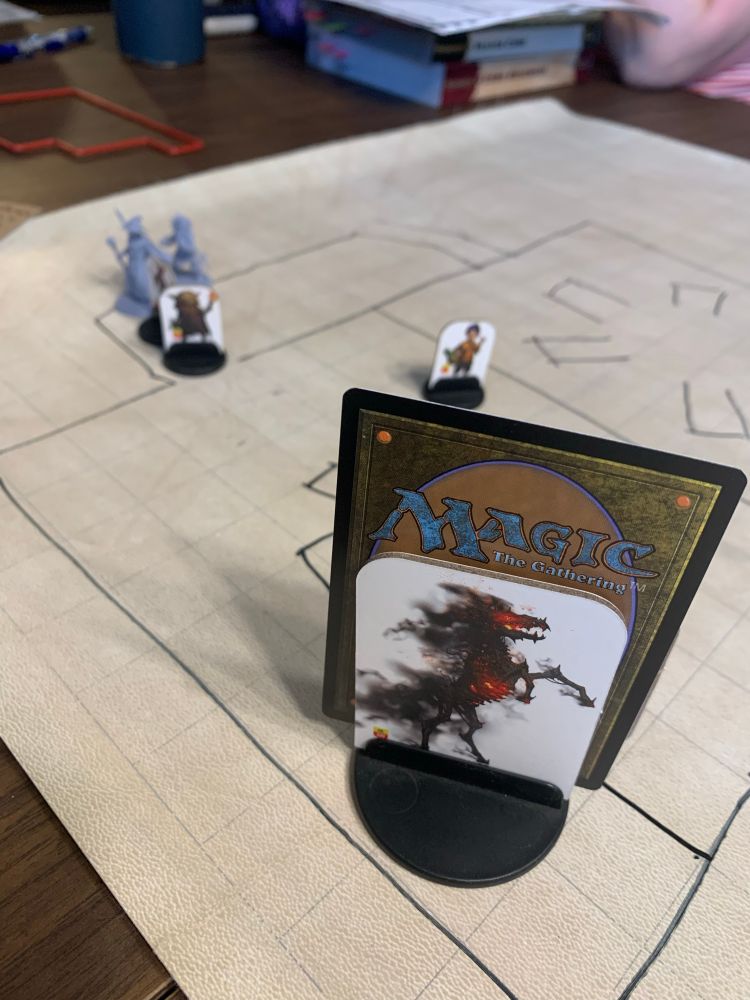 A pathfinder game board. Minis are lined up to go into a room with a horse standee that is on fire and smoking, a Nightmare. A magic card is placed with the standee.