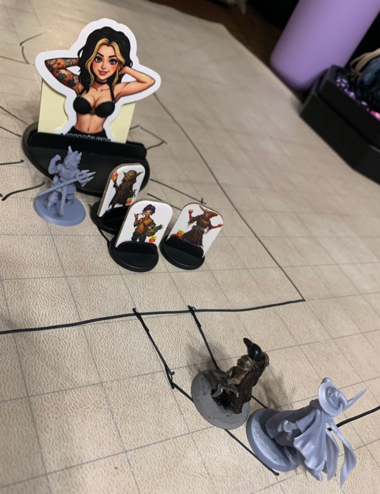 Several player character miniatures are facing off against a single enemy. The enemy placeholder is a sticker of a well-endowed woman named, “Mama Juggs”. We are losing  badly to Mama Jugs