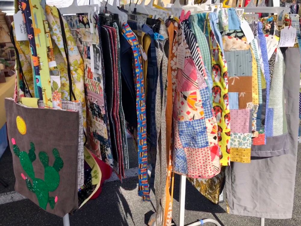 Rack full of patchwork clothing and bags and aprons set up for market. 