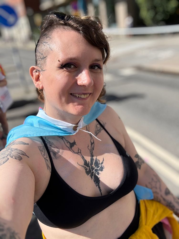 Andrea smiling with a trans flag over her shoulders and a sports bra on