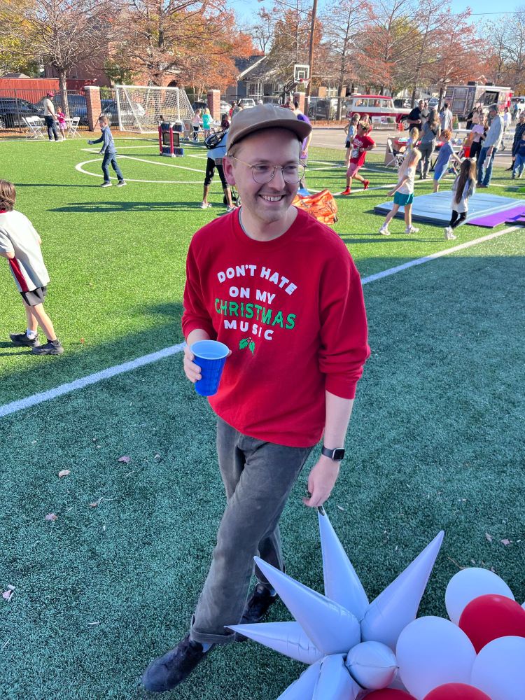 A man in a Christmas sweater with the words “Don’t Hate on my Christmas Music”