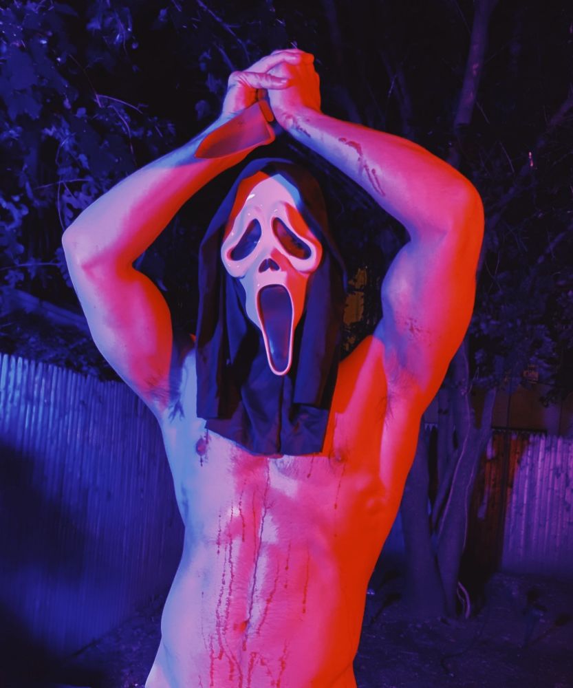 a horny bi lighting pic of ghostface, sans shirt, arms raised, knife in hand, displaying muscles in the arms and blood on the abs.