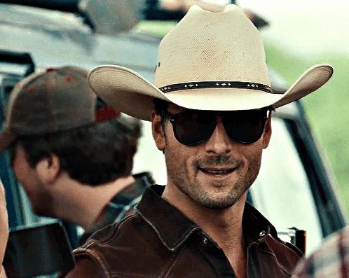 a man wearing a cowboy hat and sunglasses looks at the camera