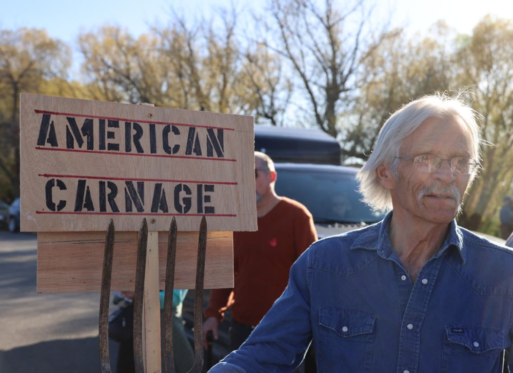 American Carnage sign on wood
White haired man wearing glasses, blue denim snap shirt