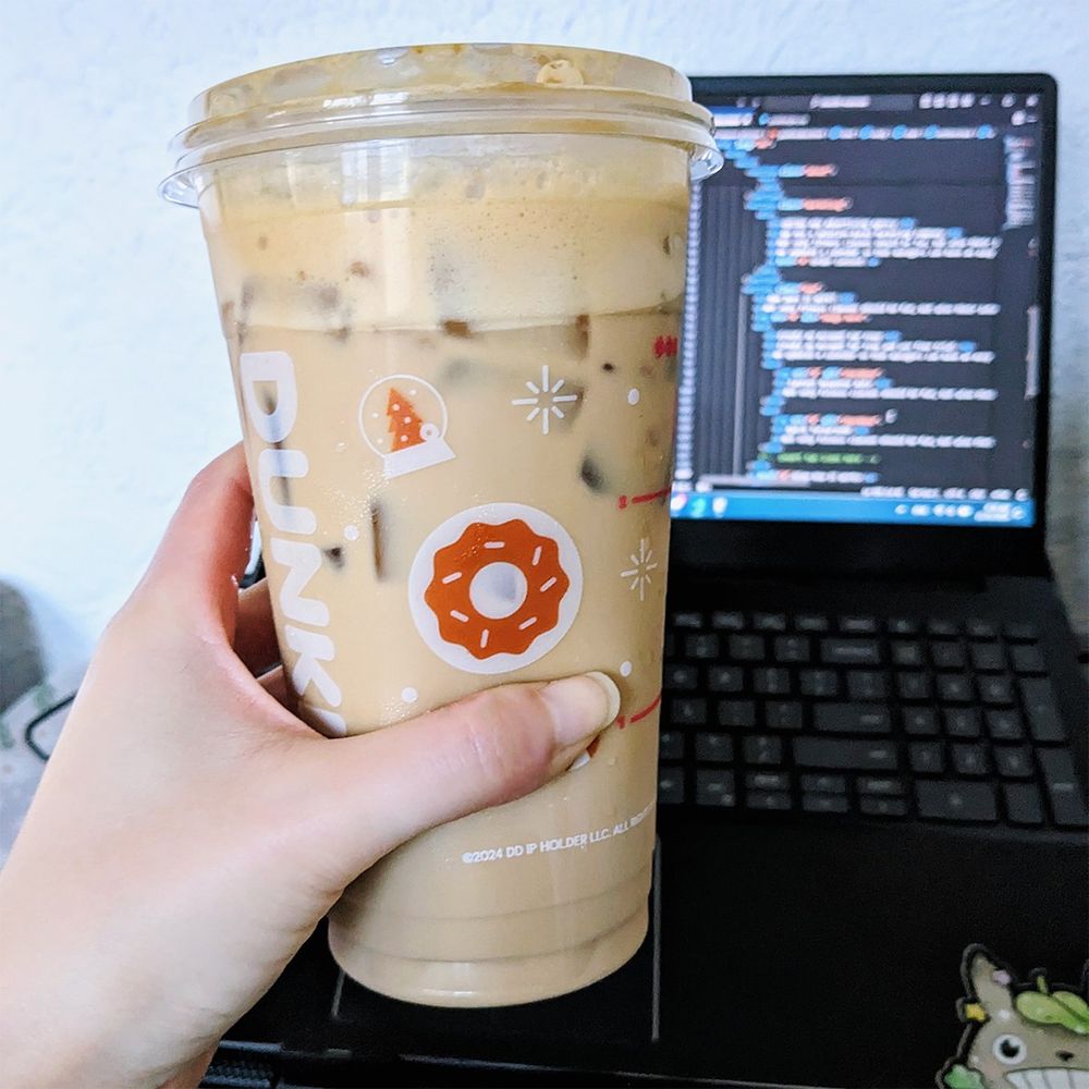 A cup of iced coffee and my laptop screen in the background with VS Code pulled up