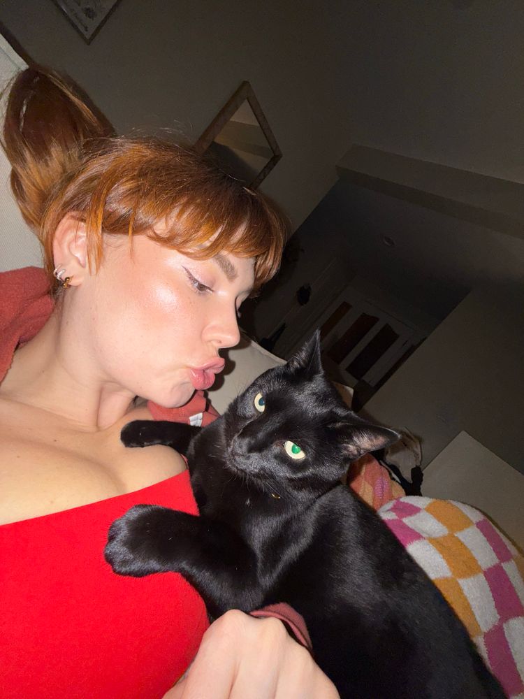 Lenny Beans, a black cat, rests on Siri’s chest while she makes a kissy face at him 