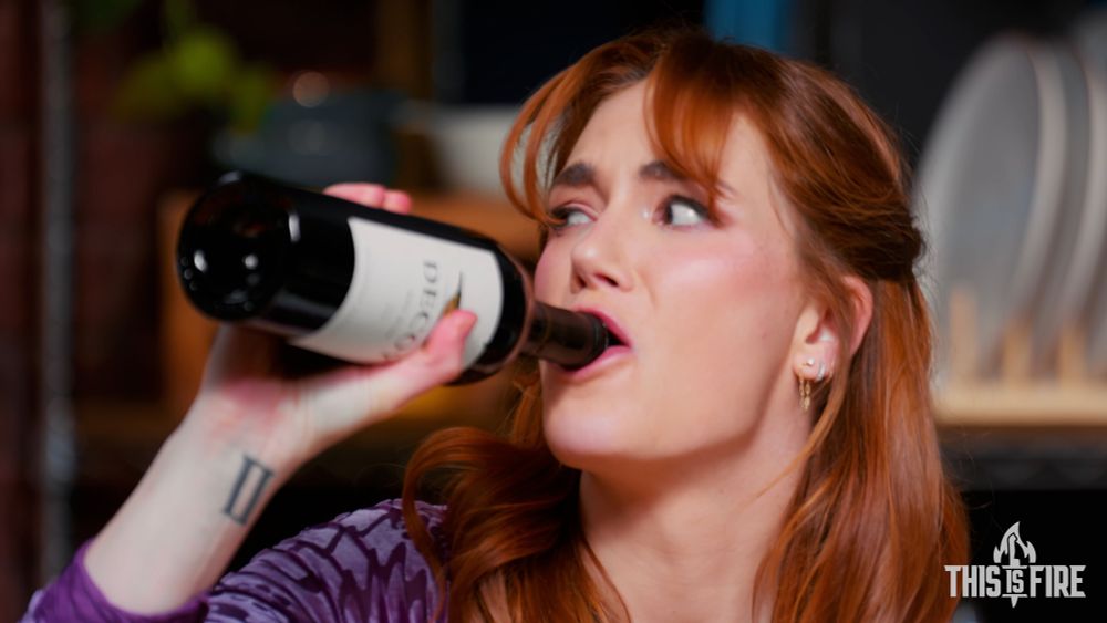 Still from “This Is Fire” of Siri looking very stressed while drinking directly from a bottle of red wine 