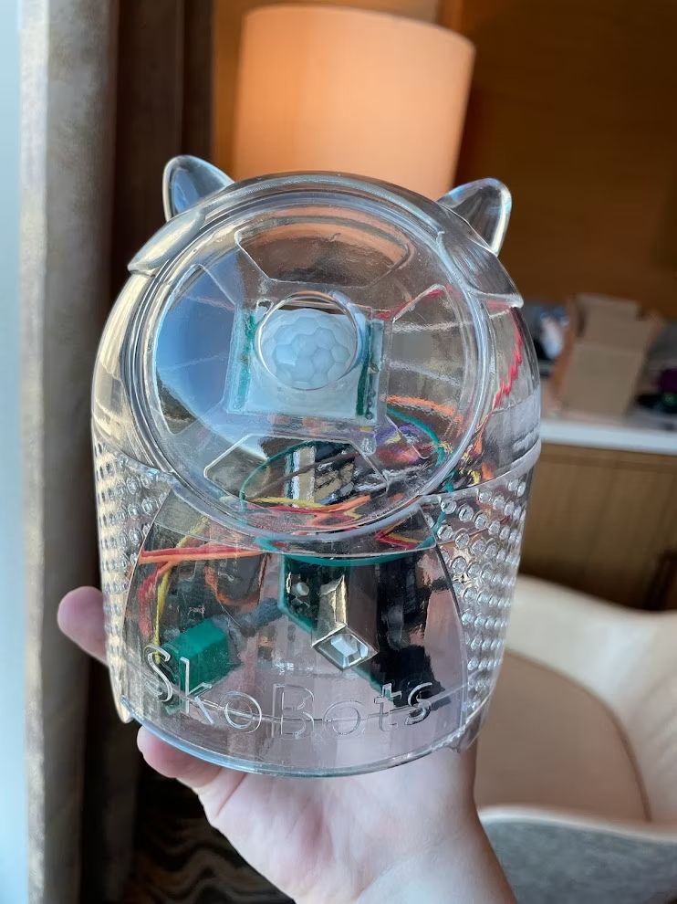 A small, clear robot being held in someone's hand. Inside the robot are some electronic components and wires.