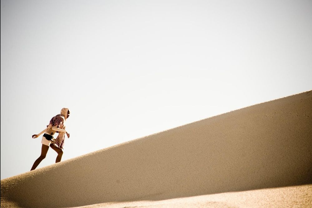 Still from "Pumzi", a short film by Wanuri Kahiu. A figure climbs a sand dune against a grey sky.