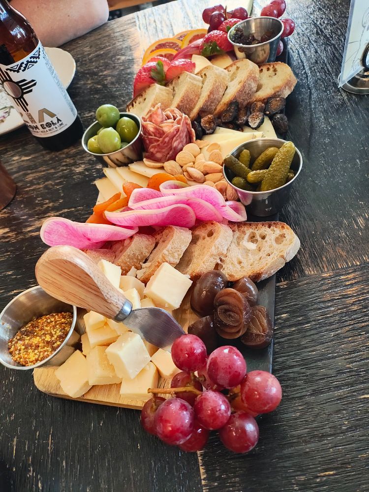 Photo of a Charcuterie board, four cheeses, meat, olives, figs, bread, cremini onions, watermelon radish, red grapes, blood orange,figs, gala apples, marcona almonds, dried apricots, cornichons, strawberries, mustard, and fig marmalade.