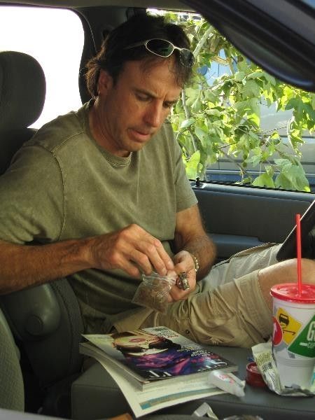 Still from the television show Weeds showing Kevin Nealon packing a bowl from a bag of weed in his car