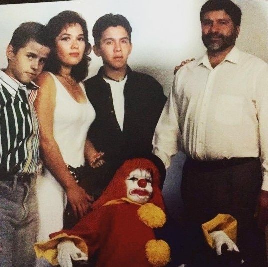 A family photo showing a family of five two brothers the mother and father standing in the back with a child dressed as a clown sitting in front of them leaned back looking tough