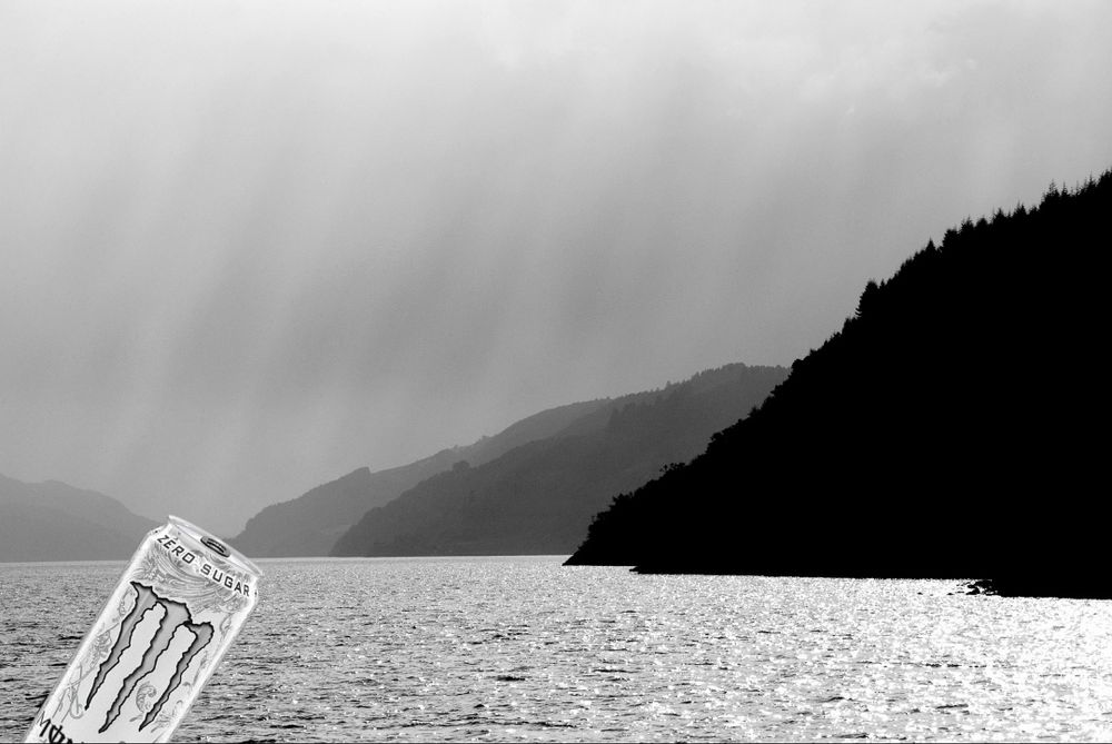 A black and white photo of Loch Ness in Scotland with a can of white Monster energy in the bottom left corner
