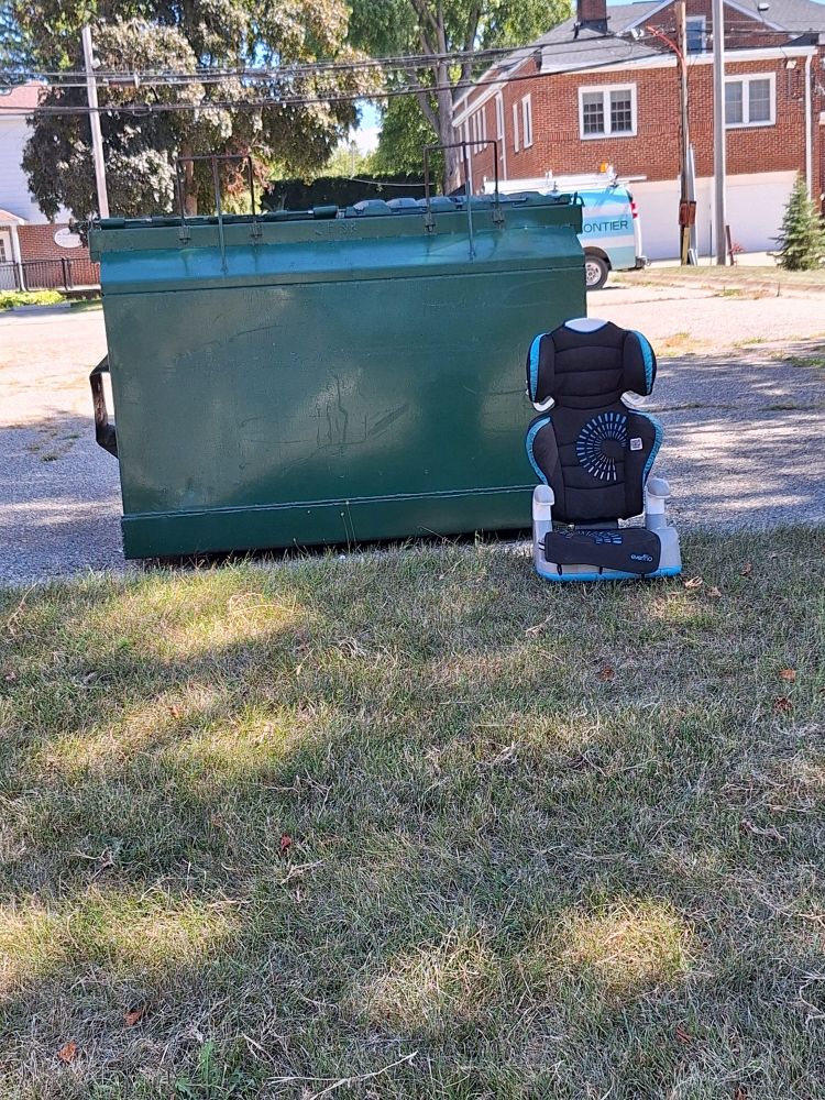 A picture I took on my walk of a dumpster with a child's cart seat sitting in front of it