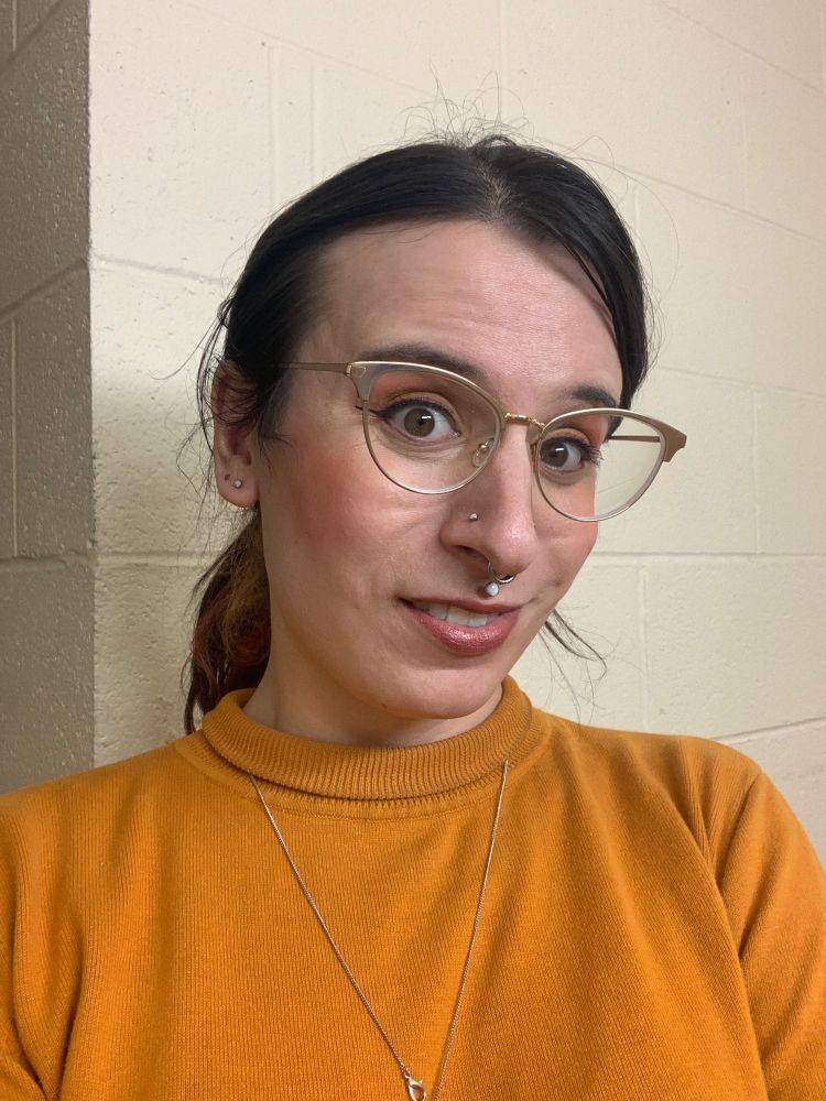 A girl with dark brown hair and glasses wearing a yellow sweater.