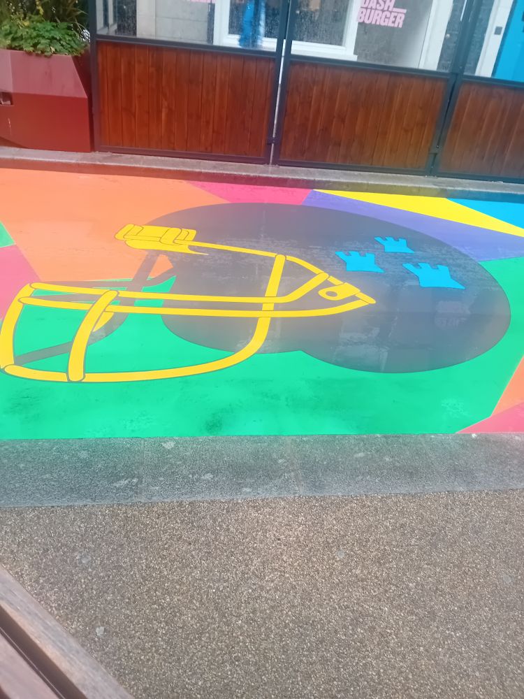 An American football helmet with the three castles that are logo of Dublin City Council on it. It's against a colourful background covering the road on Capel St, a pedestrianised street in Dublin city centre.