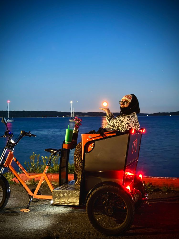 Rad burro  pedicab with Salish sea in background and my bundled up bespectacled wife holding the moon in palm 