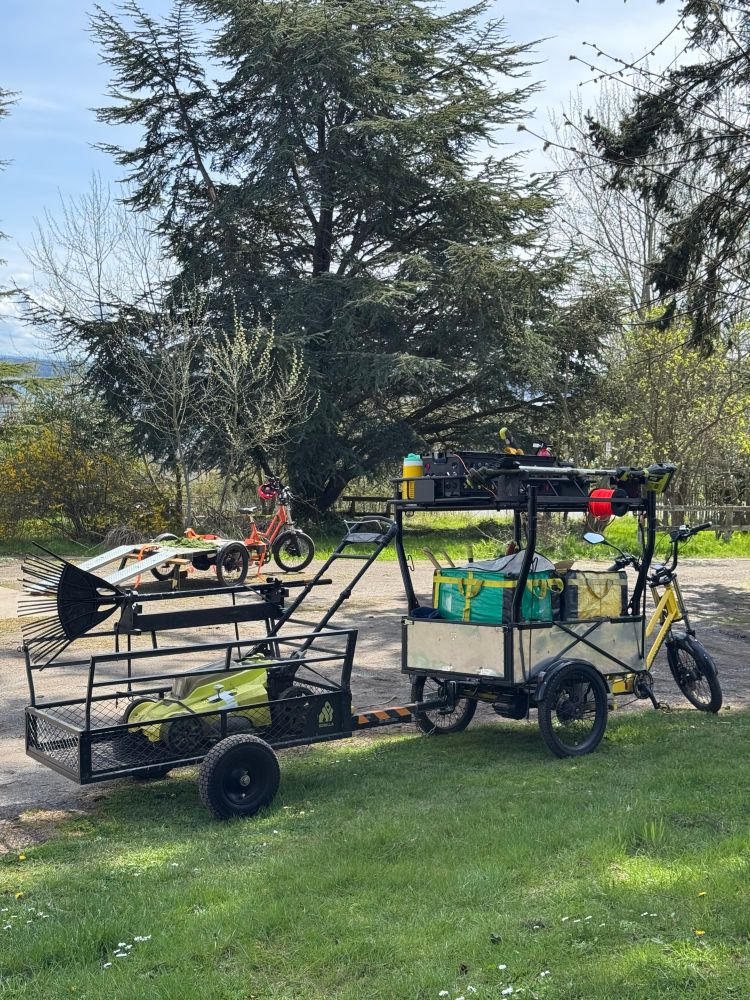 2 cargo trikes in gravel driveway, one with ramps the other with a trailer and tools 