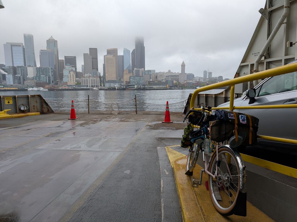 Second angle on the car deck looking out the front at the Seattle skyline, bike in the foreground viewed from the back. Low clouds obscure the your of the buildings. 