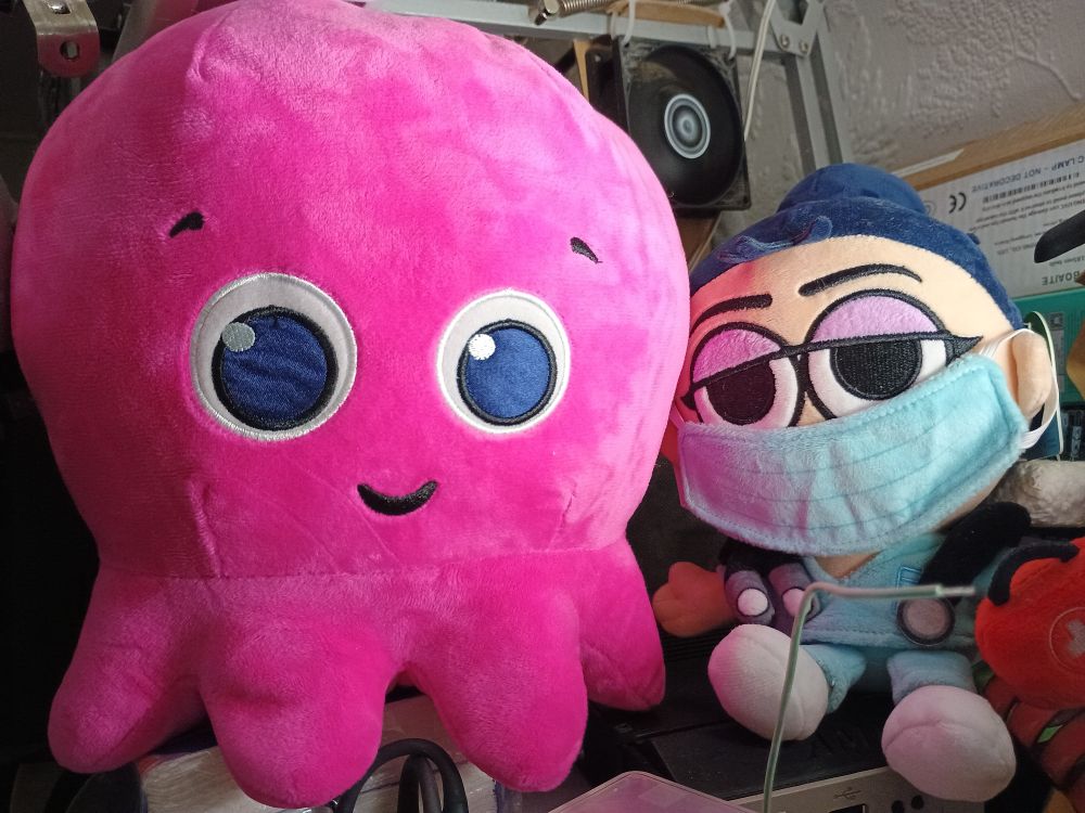 A big bright pink Octopus, called Constantine, sits beside Nurse with a blue mask on her face in blue scrubs, holding a red first aid kit.