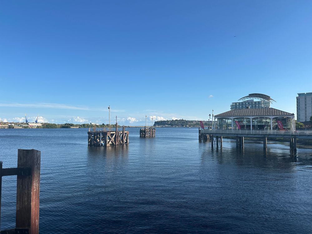 Cardiff Bay. A building on a small pier juts out from the left in the midground. Penarth headland is visible in the distance.