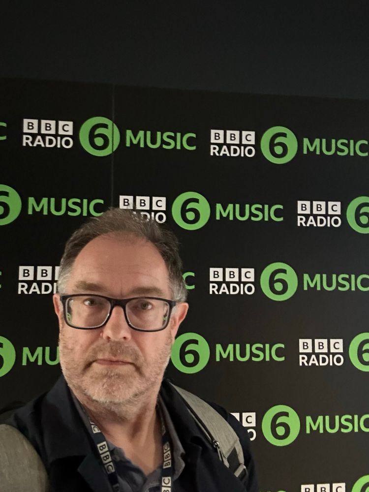 Me, wearing a BBC lanyard, standing in front of a BBC 6 Music hoarding