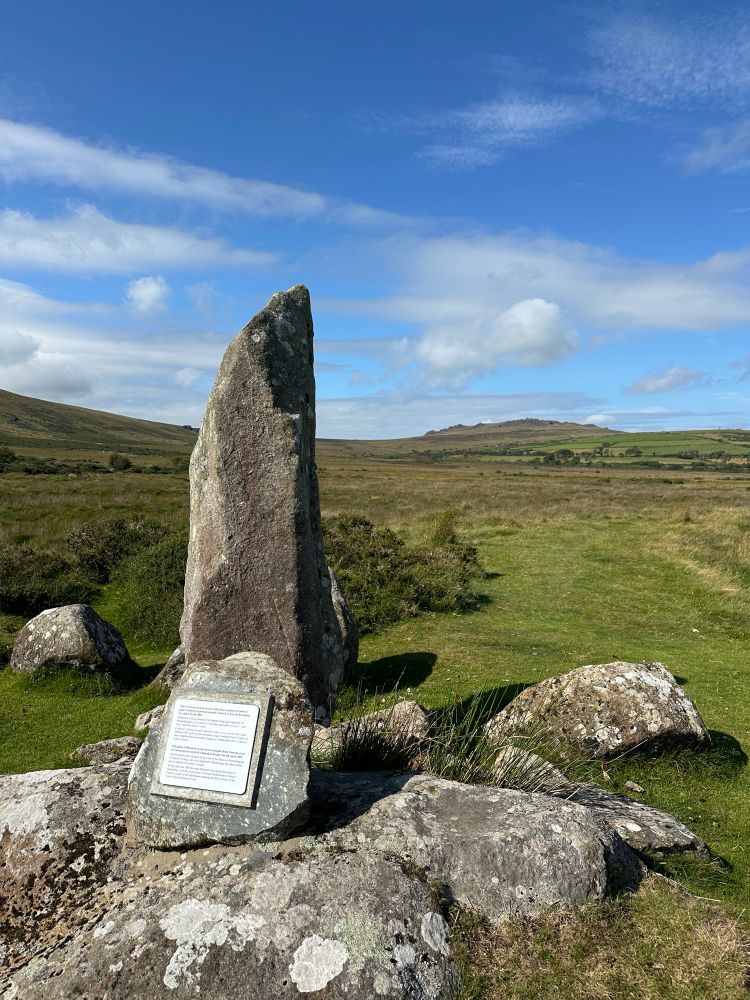 A standing stone with a plaque in front. It’s a bluestone from this area of the Preseli hills. In the distance is Foel Drygarn, a hill fort.
